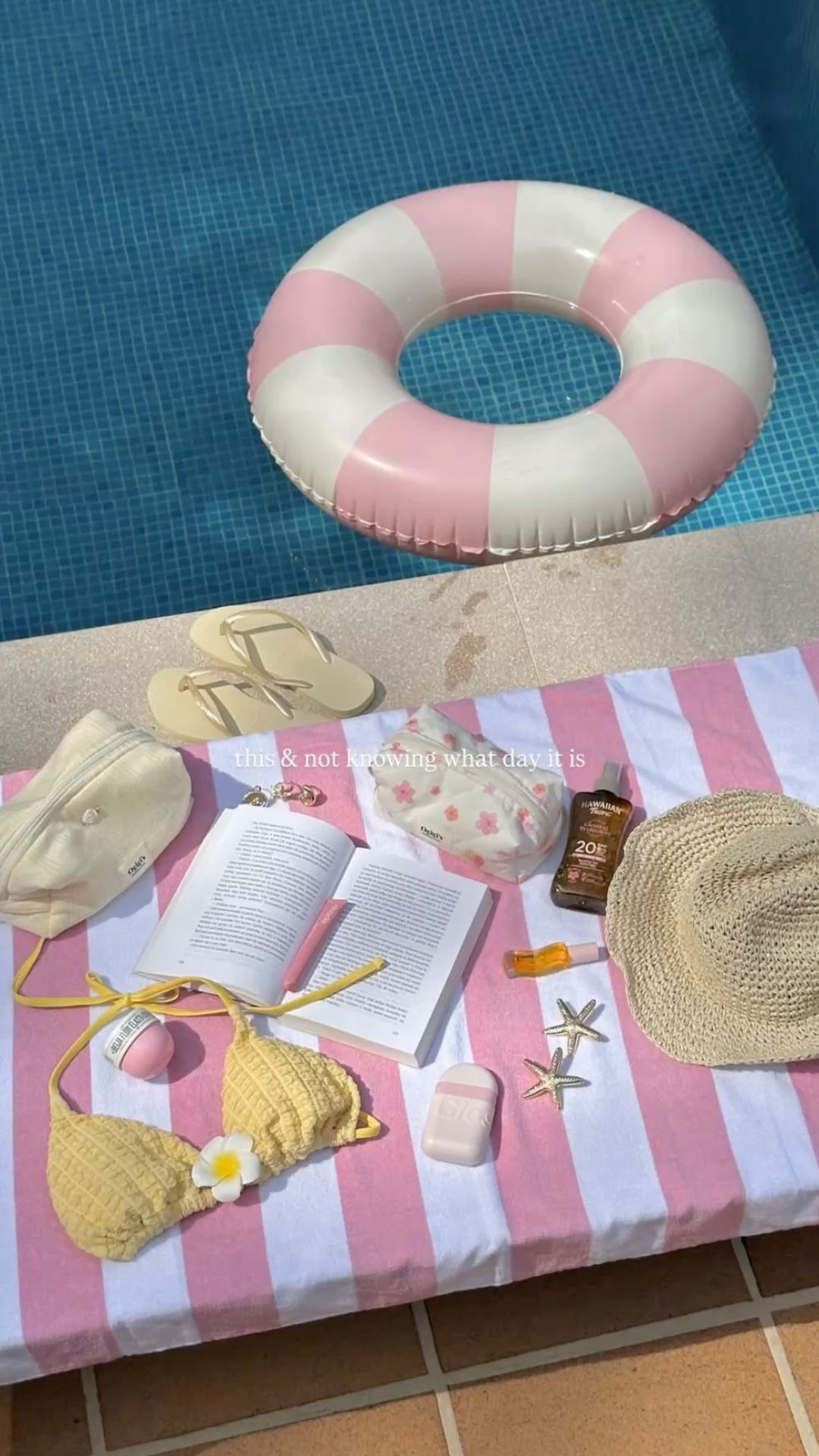 Vue du dessus d'un bikini jaune avec une fleur, un livre ouvert et des accessoires disposés sur une serviette rayé.