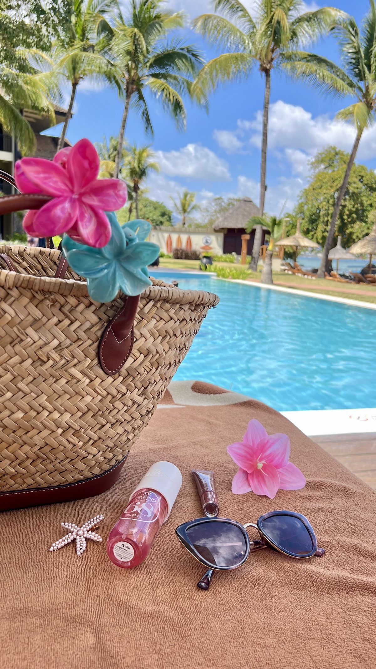 Panier en paille avec des fleurs tropicales au bord d'une piscine avec des palmiers.