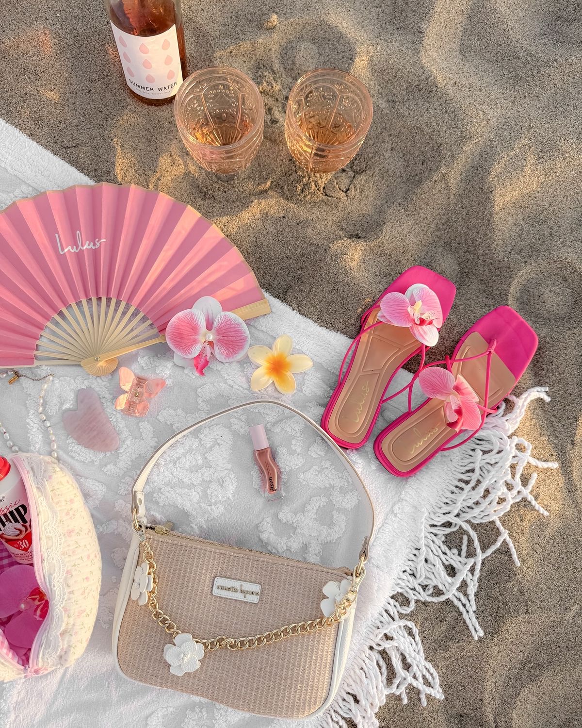 Pique-nique esthétique sur la plage avec du vin, un éventail, des sandales, un sac et des fleurs