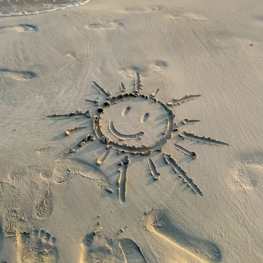 Un soleil souriant tracé à la main dans le sable humide sur une plage