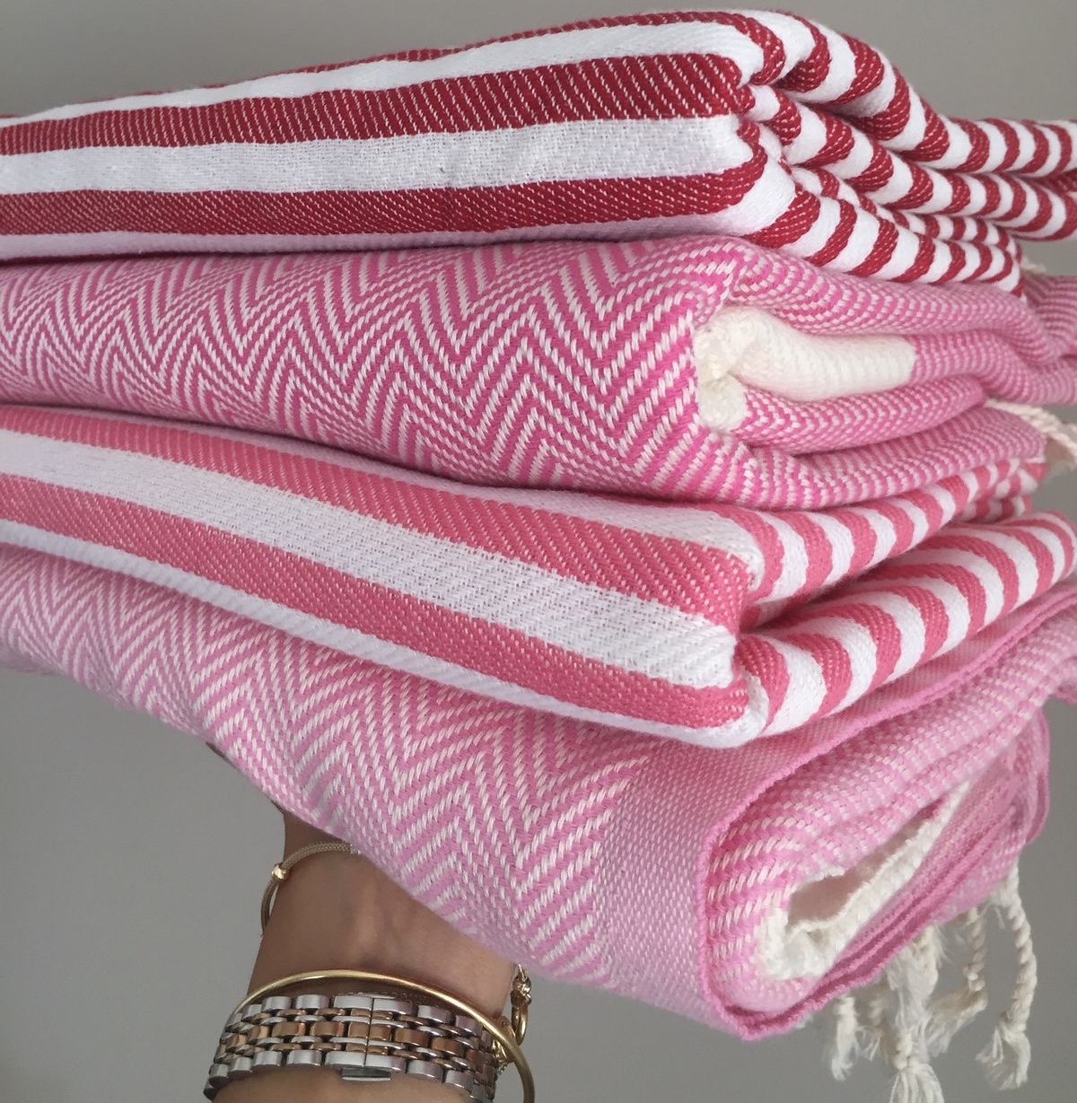 Une pile de quatre serviettes de plage dans les tons rouge, fucshia et rose.